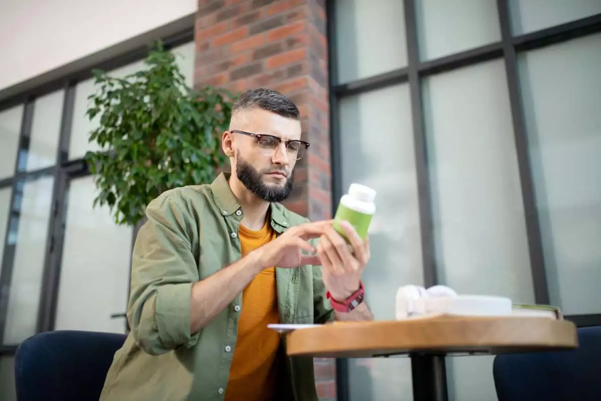 Un homme assis en train de lire l’étiquette d’une boîte de vitamines.