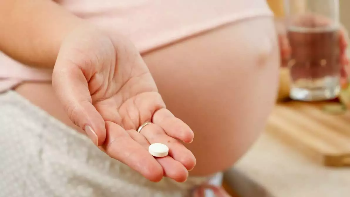 Gros plan d’une jeune femme enceinte de jumeaux qui prend un gélule de vitamine B9.