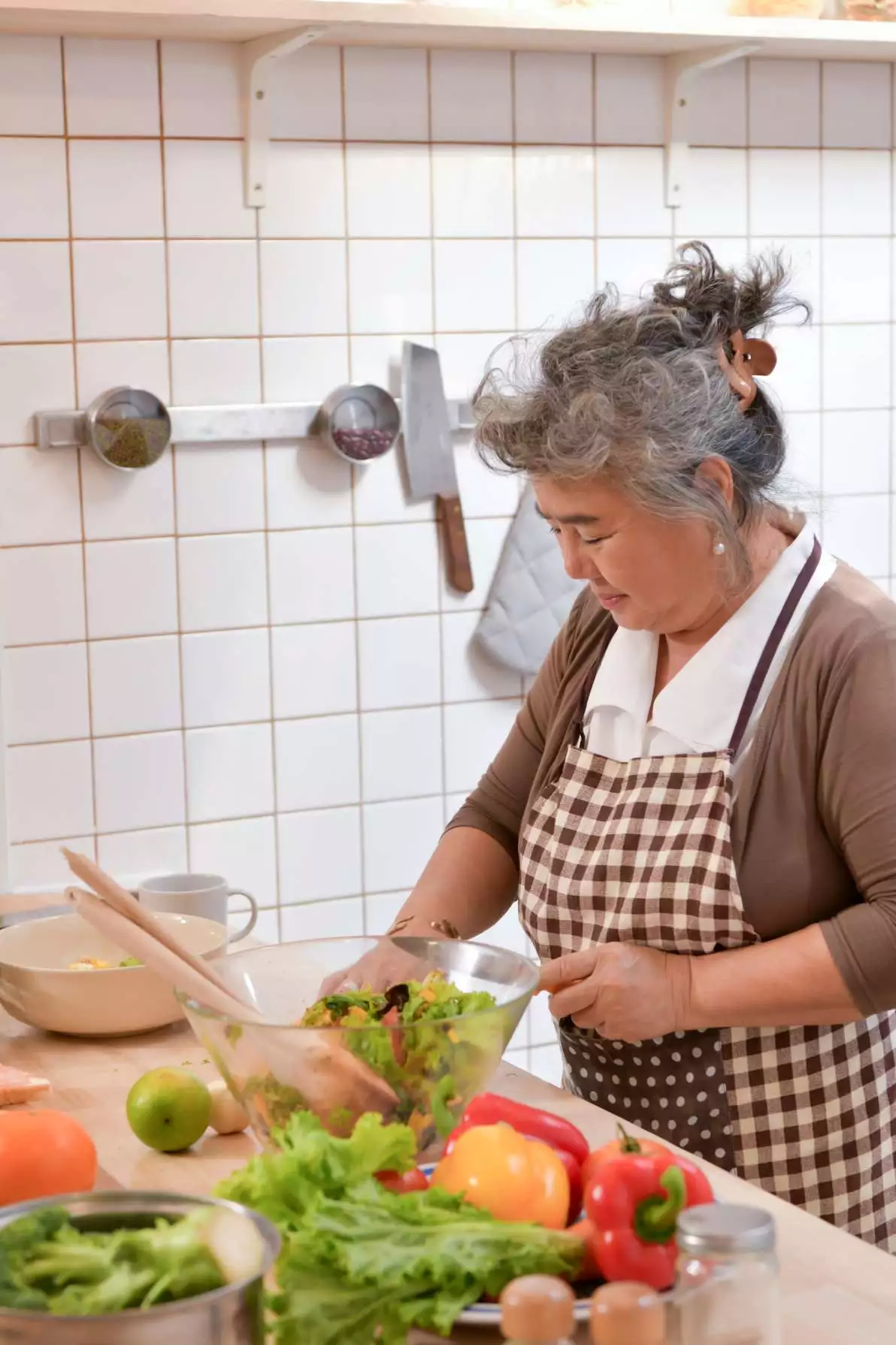 Une femme âgée cuisine un repas composé de légumes à feuilles vertes et d’oeufs, qui sont des aliments riches en vitamine B9.