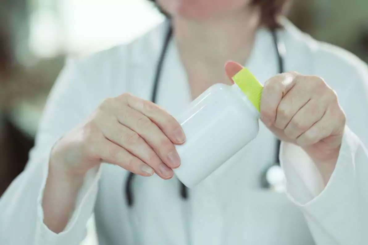 Femme médecin tenant une bouteille de compléments alimentaires dans ses mains.