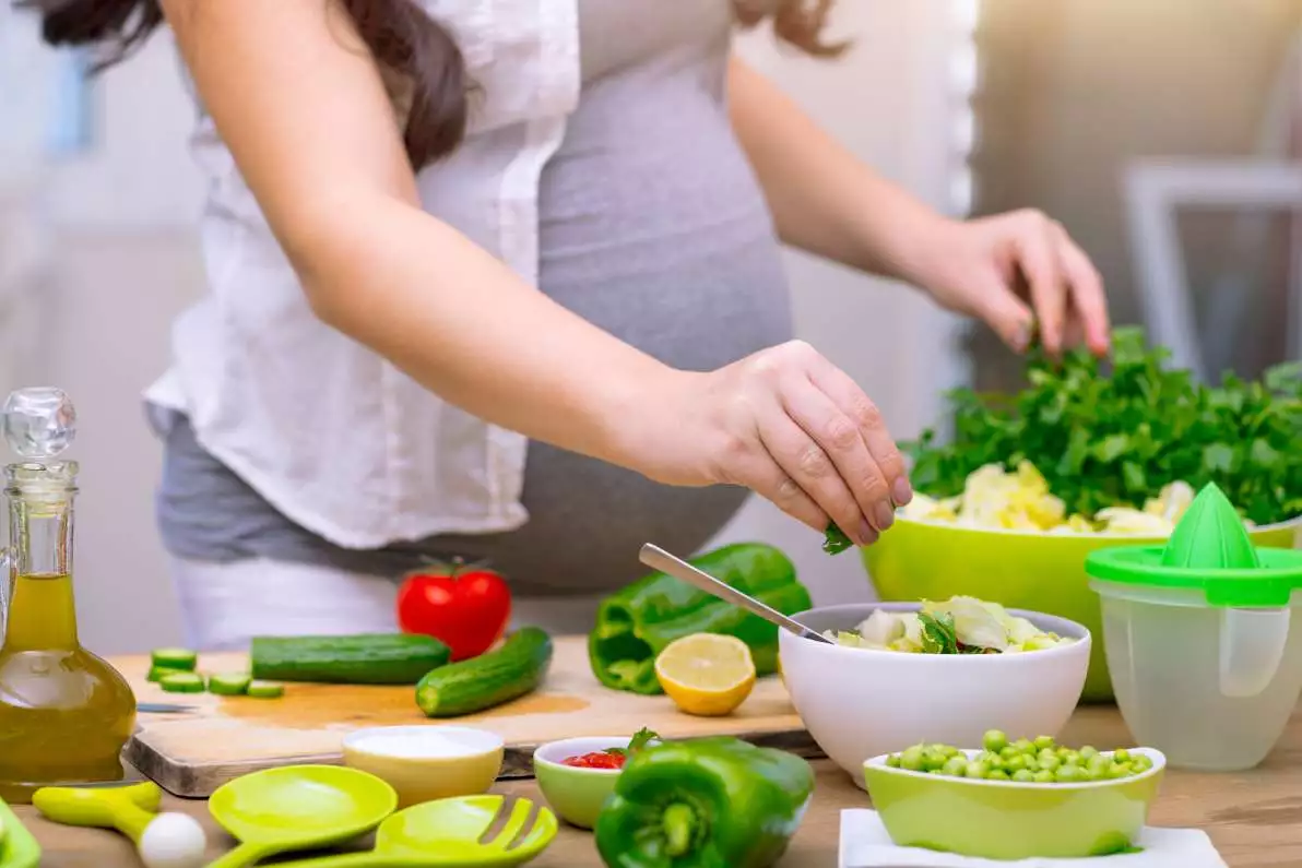 Une femme enceinte entrain de cuisiner des végétaux riches en vitamines et minéraux.