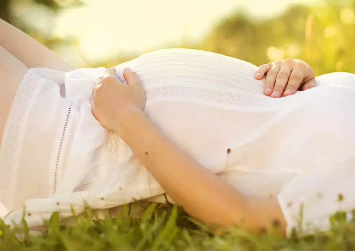 Une femme enceinte est allongée dans l’herbe.