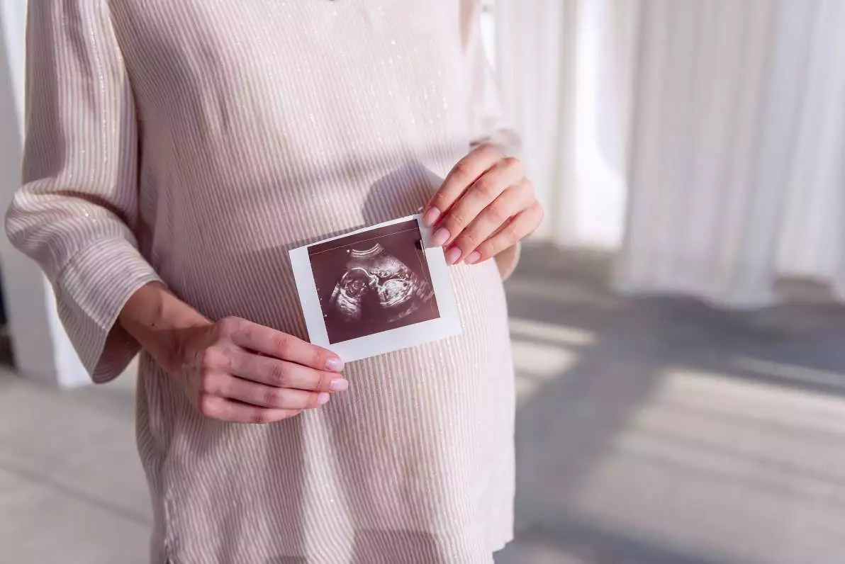 Une jeune femme enceinte tient dans ses mains une échographie morphologique.