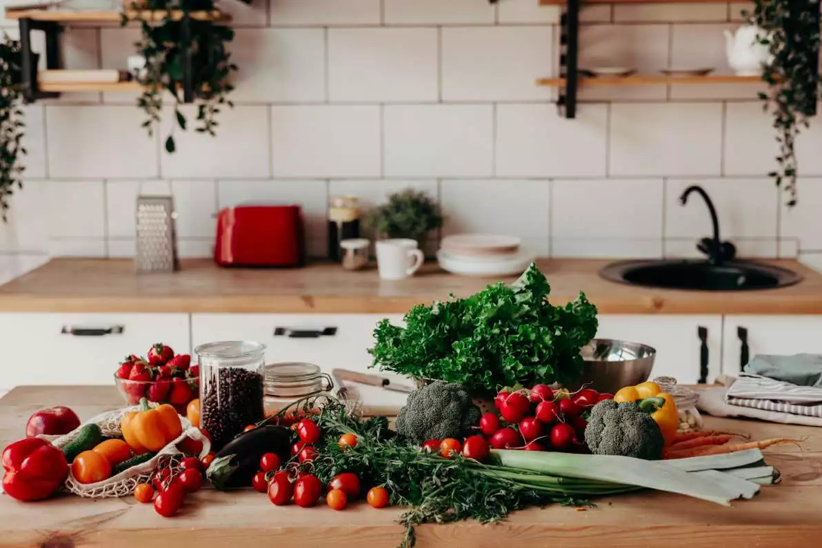 Point de vue d’une cuisine avec plein de végétaux sur la table, dont du brocoli, des tomates et de la salade.