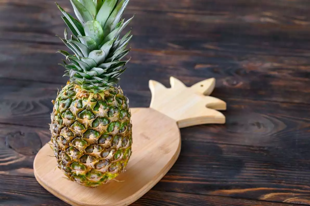 Un ananas frais posé sur une planche en bois en forme d’ananas, pour montrer sa puissance anti-inflammatoire.