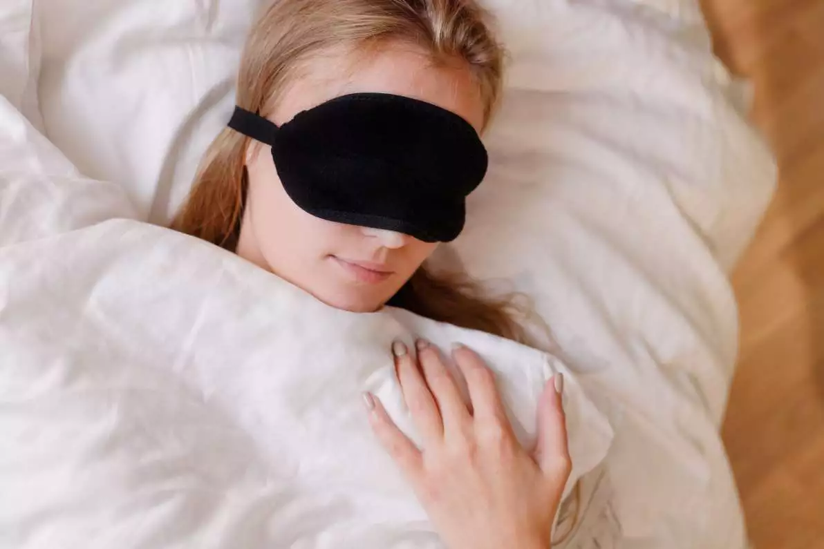 Portrait d’une jeune femme qui dort dans un lit avec un masque sur les yeux.