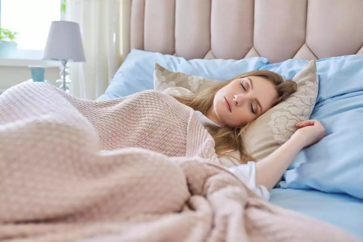 Jeune femme endormie dans un lit, entrain d’avoir un sommeil réparateur profond.