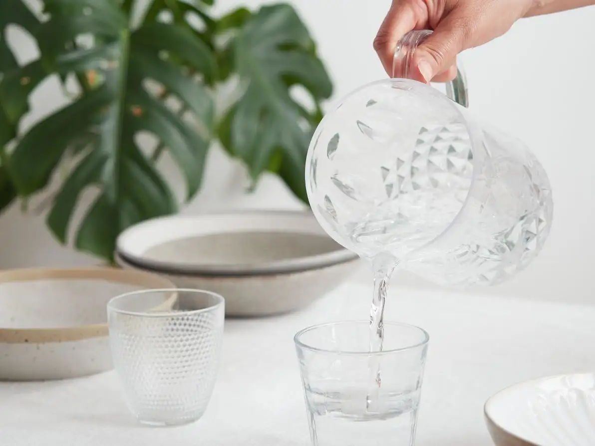 Une femme se sert de l’eau dans un verre pour bien s’hydrater pendant le repas