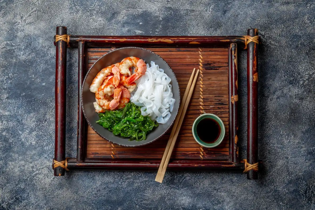 Repas servis sur un plateau composé de nouilles de konjac, de crevettes et de wakame, avec une sauce soja