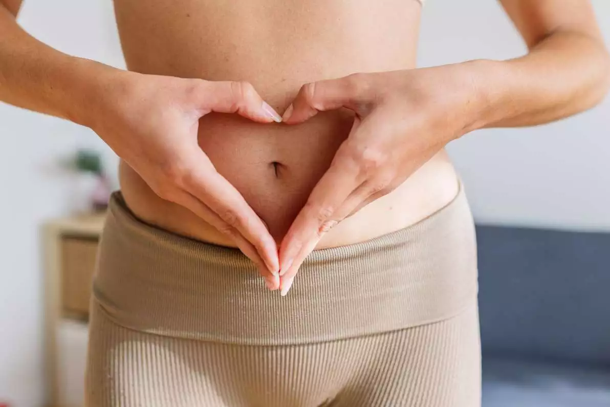 Une femme forme un cœur avec ses mains au niveau de son ventre, pour signifier de prendre soin de ses intestins.