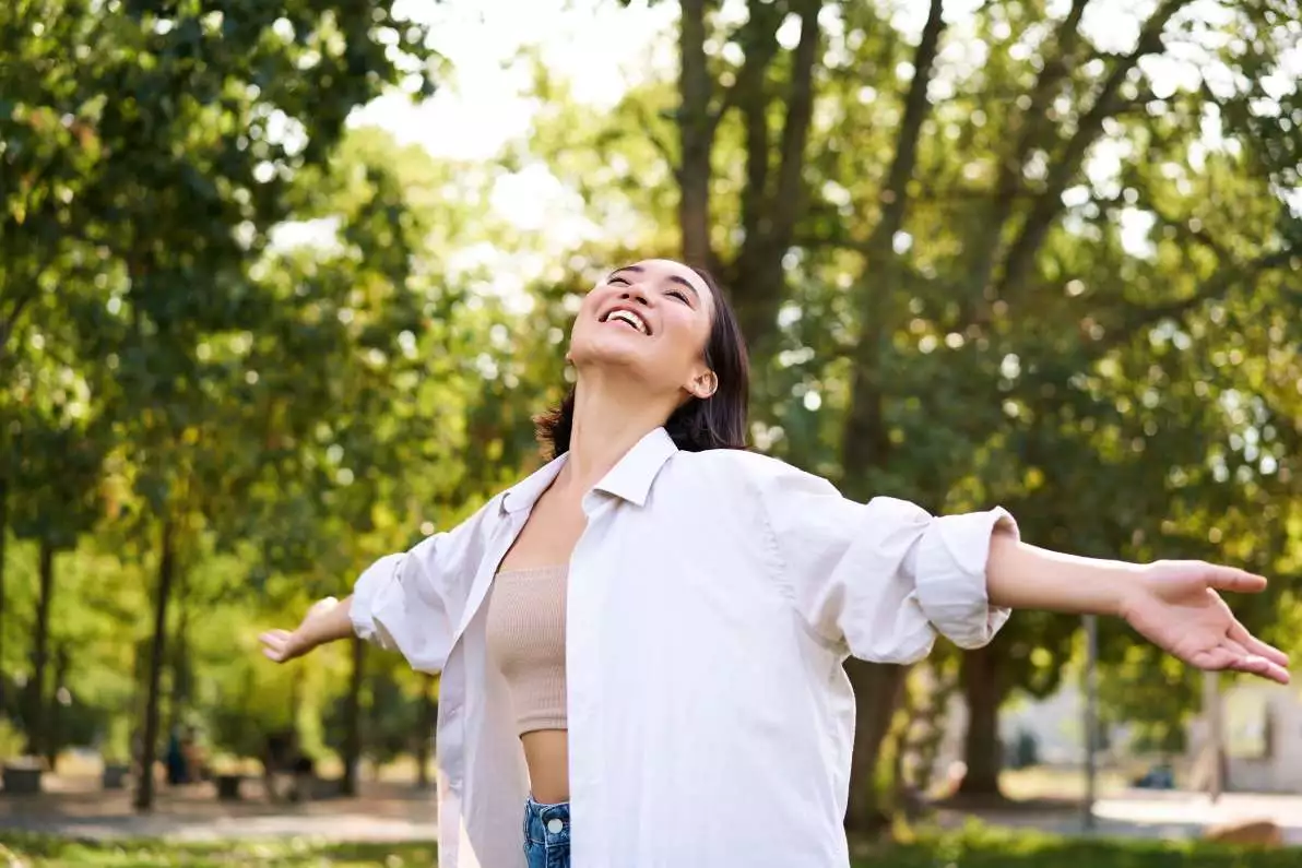 Portrait d'une jeune femme dans un parc, jouissant de la liberté et souriant de joie.