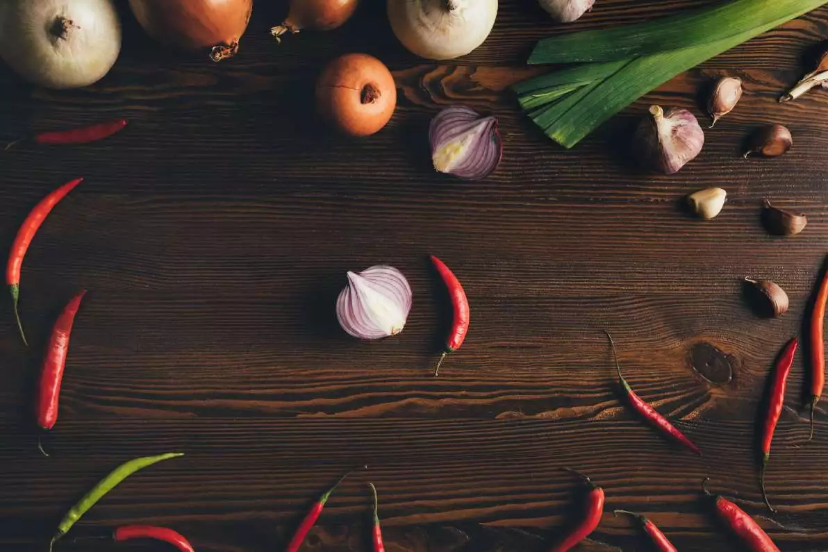 Vue du dessus de l'oignon, de l'ail et des piments sur une table en bois, qui représentent des sources de quercétine.